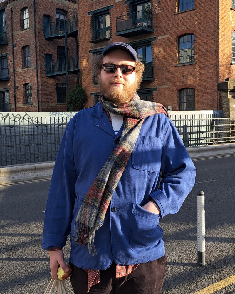 Jack in a blue work jacket and scarf outside an old brick warehouse
